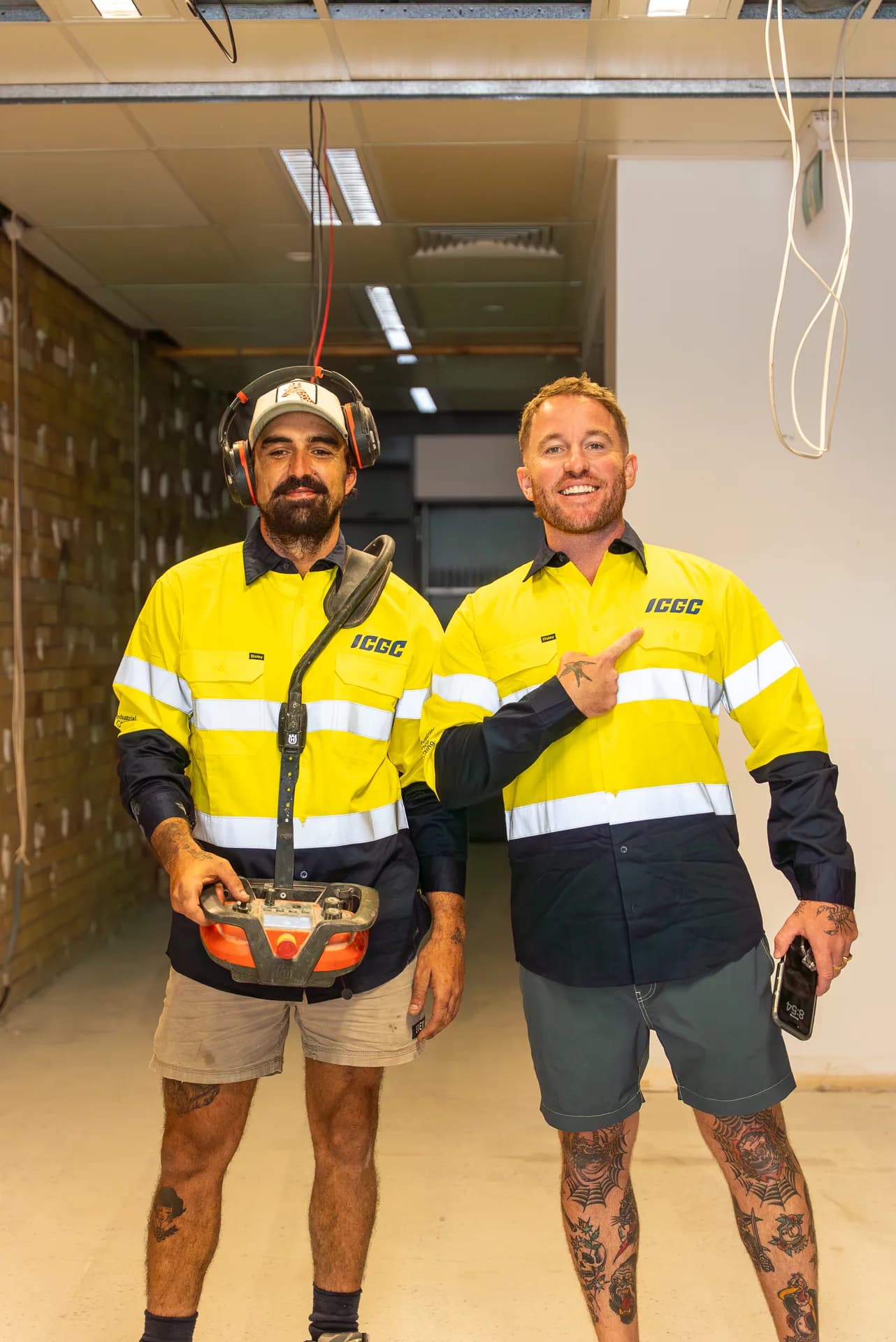 Two ICGC team members in branded yellow hi-vis uniforms at a commercial project with exposed brick walls